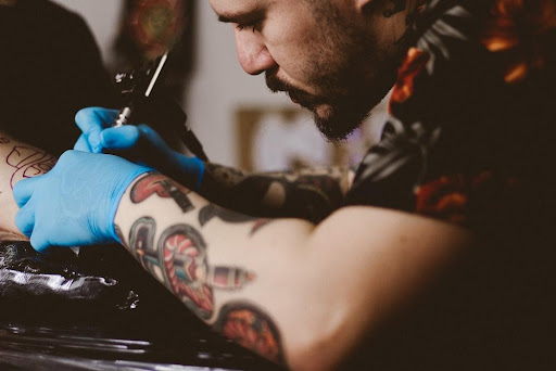 A Tattoo Artist with Colored Tattoo Designs Over Their Forearm Inking a Body Part
